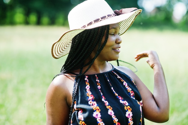 Portret przepięknej afroamerykanki 20s w letnim kapeluszu pozuje na zielonej trawie w parku