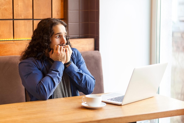 Portret przestraszony przystojny młody dorosły mężczyzna freelancer w stylu casual, siedząc w kawiarni i oglądając horrory w laptopie, gryźć paznokcie, bussinessman w biurze. Koncepcja wnętrz, styl życia