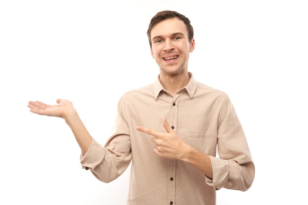 Portret przyjaznego pozytywnego młodego człowieka uśmiechającego się palcem wskazującym przy pustej przestrzeni kopii dla tekstu lub produktu na białym tle baner reklamowy