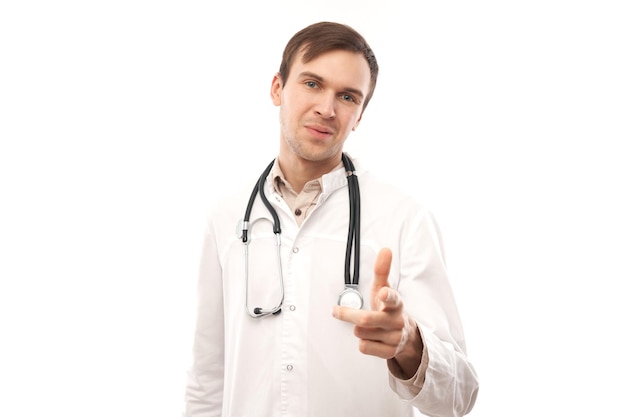 Portret przyjaznego pozytywnego młodego lekarza płci męskiej w białym fartuchu medycznym wybiera cię wskazując palcem na aparat na białym tlexA