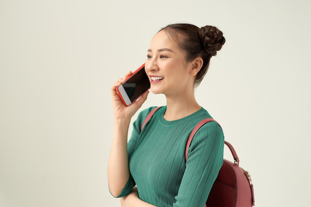 Portret przypadkowa kobieta, studentka z plecakiem trzymająca telefon komórkowy w ręku stojąca uśmiechnięta rozmawiająca na białym tle izolacja