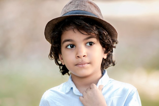 Portret przystojnego chłopca z długimi włosami, w kapeluszu na głowie i odwracającego wzrok w milczeniu.