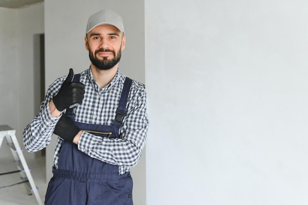 Portret przystojnego mechanika z kilkudniowym zarostem w niebieskiej koszuli ze skrzyżowanymi ramionami patrzącego w kamerę