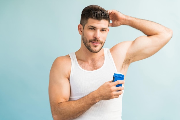 Portret przystojnego mężczyzny trzymającego dezodorant stojąc z podniesioną ręką w studio