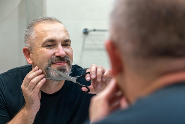 Zdjęcie portret przystojnego mężczyzny w średnim wieku, obcinającego nożyczkami brodę i wąsy