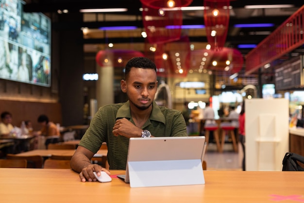Portret przystojnego młodego czarnego mężczyzny korzystającego z laptopa w kawiarni