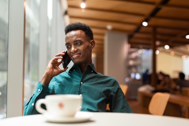 Portret przystojnego młodego czarnego mężczyzny w kawiarni przy użyciu telefonu