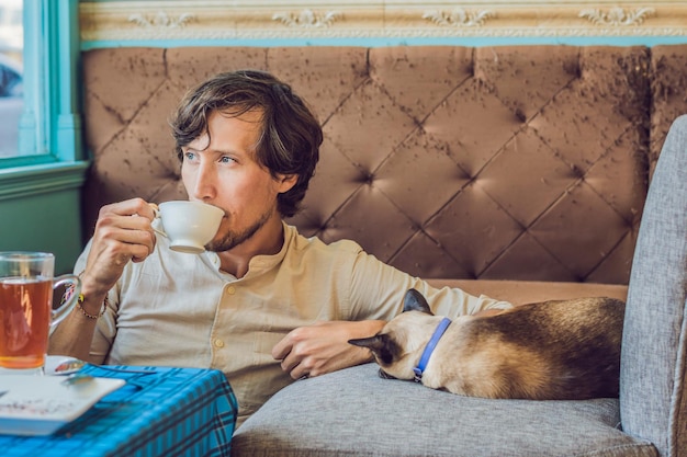 Portret przystojnego młodego mężczyzny bawiącego się kotem i pijącego kawę
