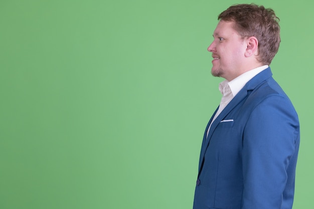 Portret przystojny biznesmen z nadwagą brodaty na sobie garnitur przeciwko klucz chroma lub zieloną ścianę