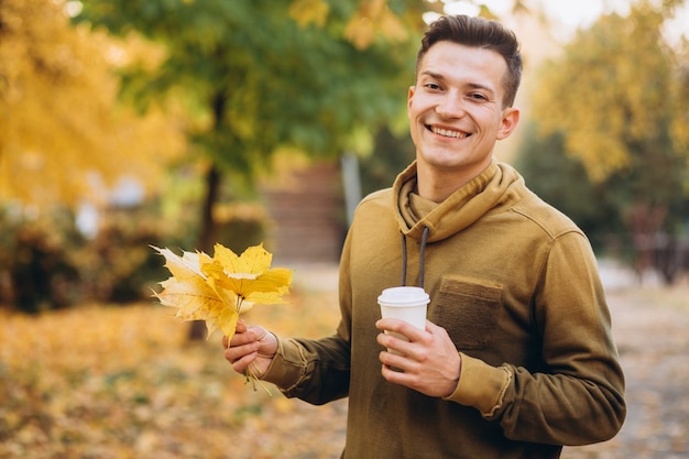 Zdjęcie portret przystojny facet, uśmiechając się i trzymając bukiet jesiennych liści i filiżankę kawy