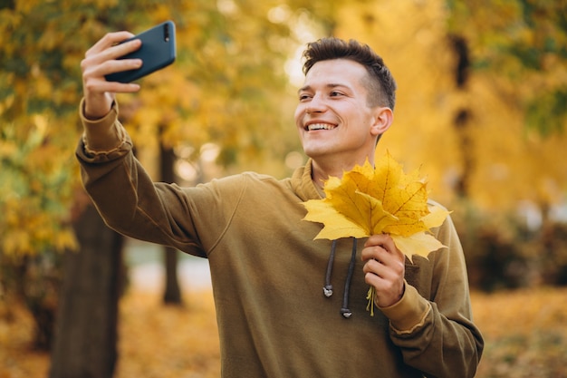 Portret przystojny facet z bukietem jesiennych liści i biorąc selfie