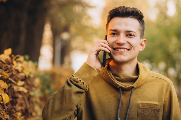Portret przystojny i szczęśliwy facet uśmiecha się i rozmawia przez telefon w jesiennym parku