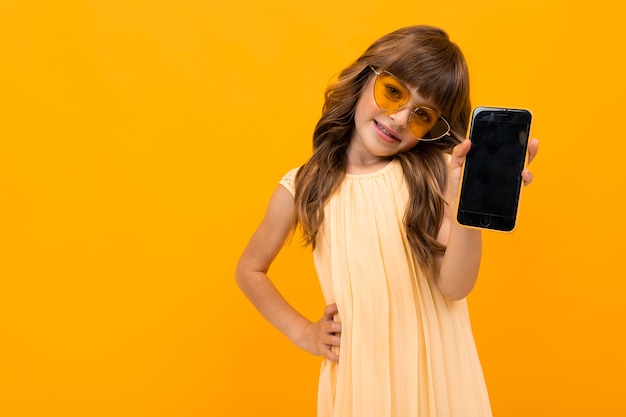 Portret przystojny kaukaski dziewczyna z długimi kasztanowymi włosami i ładną buzią w bieli i sukni pokazuje jej nowy smartfon i uśmiecha się