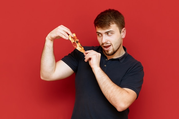 Portret przystojny mężczyzna z brodą stoi z kawałkiem pizzy w jego rękach