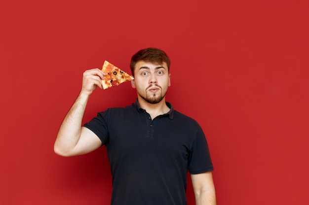 Portret przystojny mężczyzna z brodą stoi z kawałkiem pizzy w jego rękach