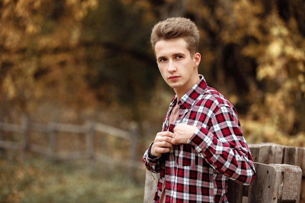 Portret przystojny młody facet w koszuli w kratę, patrząc w kamerę na tle jesiennych liści