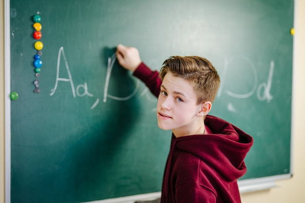 Portret przystojny młody męskiego ucznia writing na chalkboard