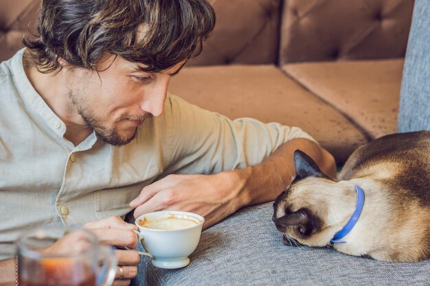 Portret przystojny młody mężczyzna bawi się kotem i pije kawę.
