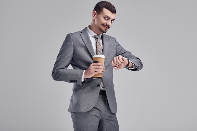 Portret przystojny młody ufny arabski biznesmen z galanteryjnym wąsem w moda szarym pełnym kostiumu trzyma filiżankę kawy w jego rękach