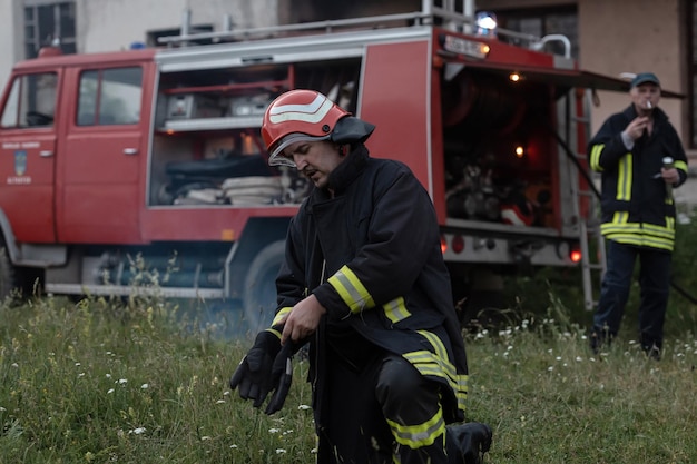 portret przystojny przygnębiony i zmęczony strażak w pobliżu wóz strażacki. Zdjęcie wysokiej jakości