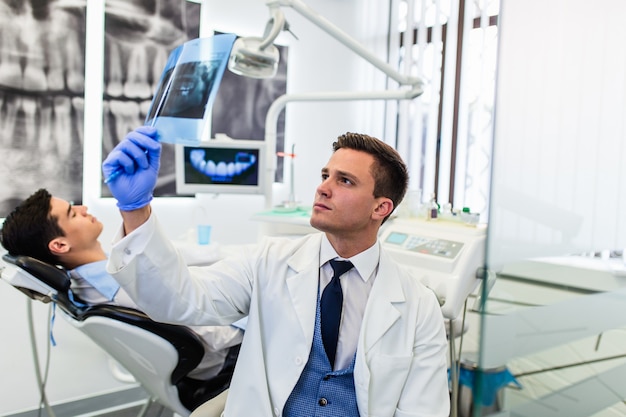Portret przystojny uśmiechający się dentysta patrząc na zdjęcie rentgenowskie swojego pacjenta.