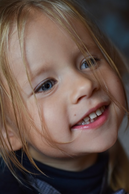 Portret radosna romantyczna mała dziewczynka z dużymi niebieskimi oczami i otwartym uśmiechem od Europa Wschodnia, zakończenie, ciemny tło