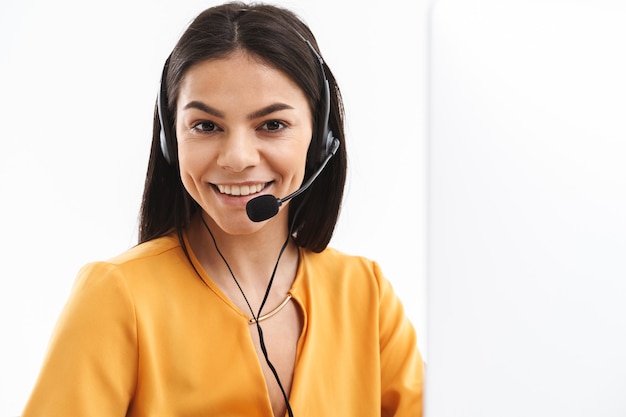Portret radosnej asystentki infolinii noszącej zestaw słuchawkowy mikrofonu rozmawiającego z klientem przez telefon podczas pracy w biurze