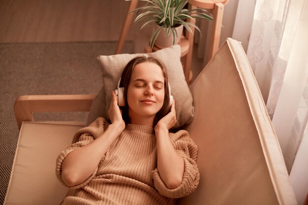 Zdjęcie portret radosnej zrelaksowanej kaukaskiej młodej kobiety słuchającej muzyki podczas odpoczynku na kanapie w domu ma zamknięte oczy, będąc spokojnym i szczęśliwym, ciesząc się ulubioną piosenką
