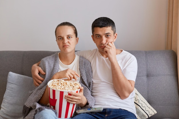 Portret rodziny żony i męża siedzących na kanapie w salonie i oglądających nudny film wyrażający nudne emocje wybierający nieciekawy film spędzający czas razem