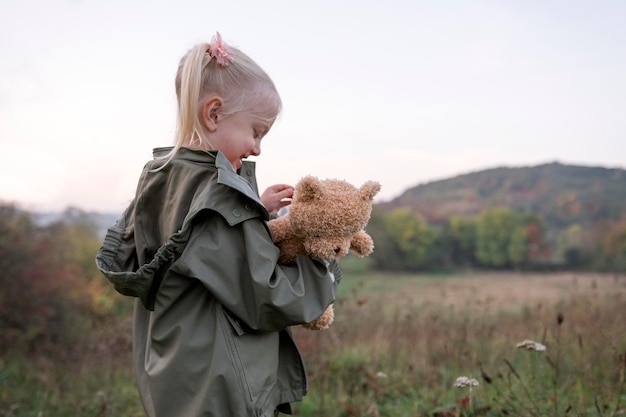 Portret roześmianej dziewczyny z małą pluszową zabawką w rękach Dziecko chodzi na polanie w górzystym terenie