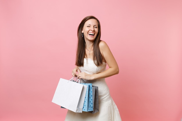 Portret roześmianej kobiety w koronkowej białej sukni, trzymającej wielokolorowe torby z zakupami po zakupach