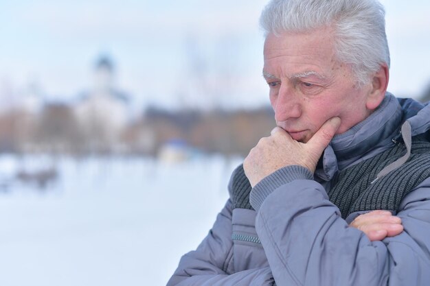 Portret rozważnego starszego mężczyzny w pokrytym śniegiem zimowym parku