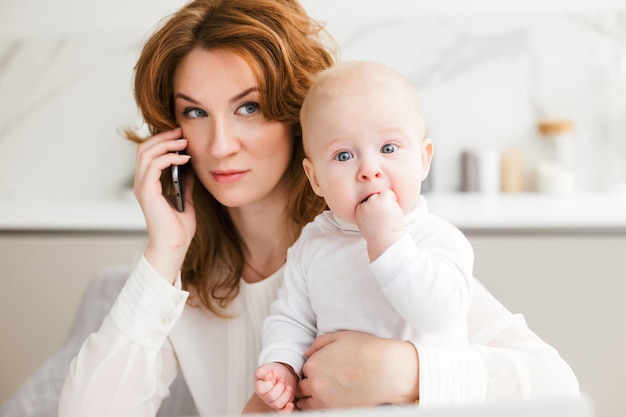 Portret rozważnej kobiety biznesu siedzącej i rozmawiającej na swoim telefonie komórkowym, trzymając w ręku swoje słodkie małe dziecko