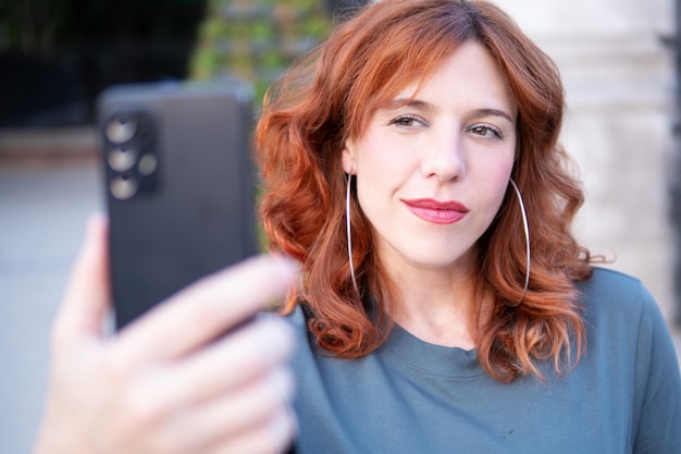 Zdjęcie portret rudej kobiety na zewnątrz z przednim aparatem telefonu komórkowego robi selfie