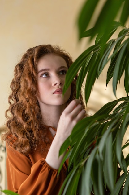 Portret rudowłosej nastolatki z kręconymi włosami na tle zielonych roślin
