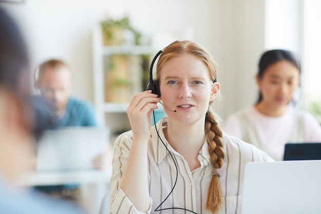Portret rudowłosy operator w słuchawkach podczas rozmowy z klientem w biurze