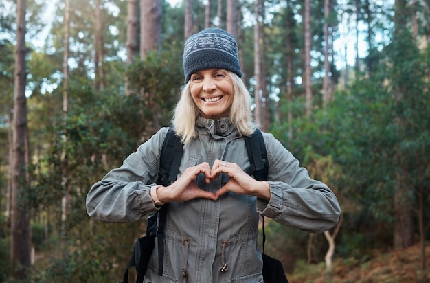 Portret serca i szczęśliwa kobieta w lesie piesze wędrówki fitness i wsparcie zdrowotne samoopieka ręce i trening sercowo-naczyniowy Podróż w przyrodzie lub trekking dojrzałej osoby w lesie ze znakiem miłości lub emoji