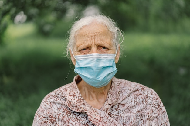 Portret siwowłosej, smutnej staruszki samotnie noszącej maskę ochronną podczas kwarantanny Covid-19.