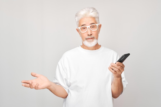 Portret siwych włosów mężczyzny w białej koszulce patrzy na telefon komórkowy i myśli Osoba ze smartfonem odizolowana na białym tle