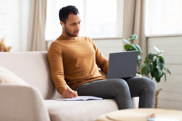 Portret skupionego Araba używającego laptopa robiącego notatki