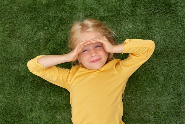 Zdjęcie portret śliczna blondynka oczy leżące na zielonej trawie mock up żółtą koszulkę widok z góry