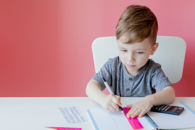 Portret śliczna Dzieciak Chłopiec Robi Pracie Domowej W Domu. Mały Skoncentrowany Dziecko Pisze Z Kolorowym Ołówkiem, Indoors. Szkoła Podstawowa I Edukacja.