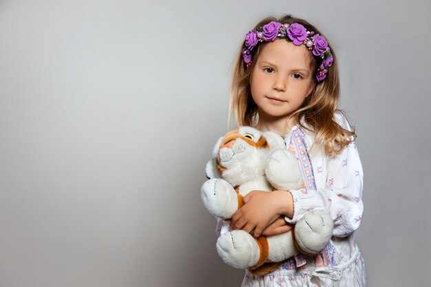 Zdjęcie portret śliczna mała dziewczynka w biel sukni i purpurowym wianku z pluszową tygrysią zabawką