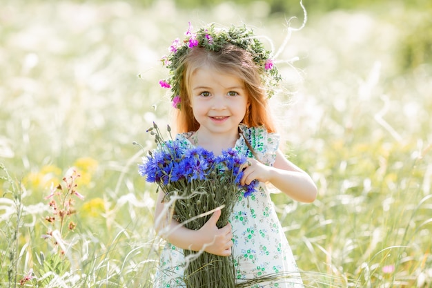 Portret śliczna mała dziewczynka z wiankiem na jej głowie uśmiecha się trzymający wildflowers chabrowego