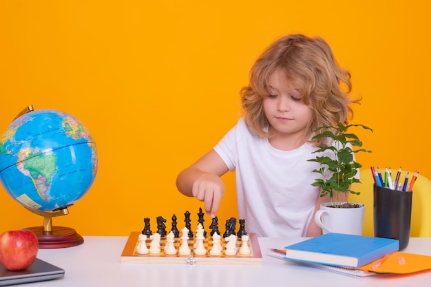 Portret ślicznego dziecka bawić się szachy na pracownianym odosobnionym tle dziecko myśli blisko szachownicy nauczyć się