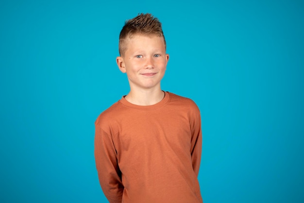 Zdjęcie portret ślicznego uśmiechniętego chłopca preteen stojącego na niebieskim tle w studio