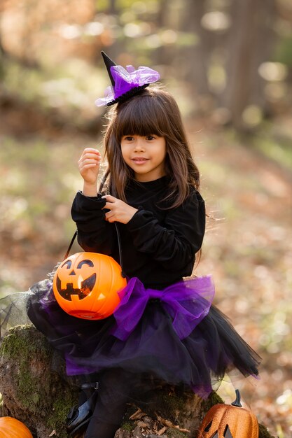 portret ślicznej brunetki w czarnej halloweenowej sukience z koszem na słodycze