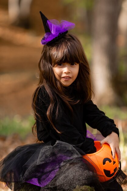 portret ślicznej brunetki w czarnej halloweenowej sukience z koszem na słodycze