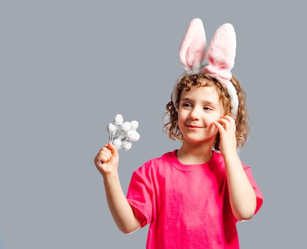 Portret ślicznej małej dziewczynki noszącej uszy wielkanocnego królika i trzymającej małe jajka