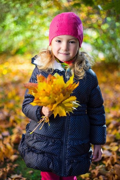 Portret ślicznej małej dziewczynki z liśćmi klonu w jesiennym parku